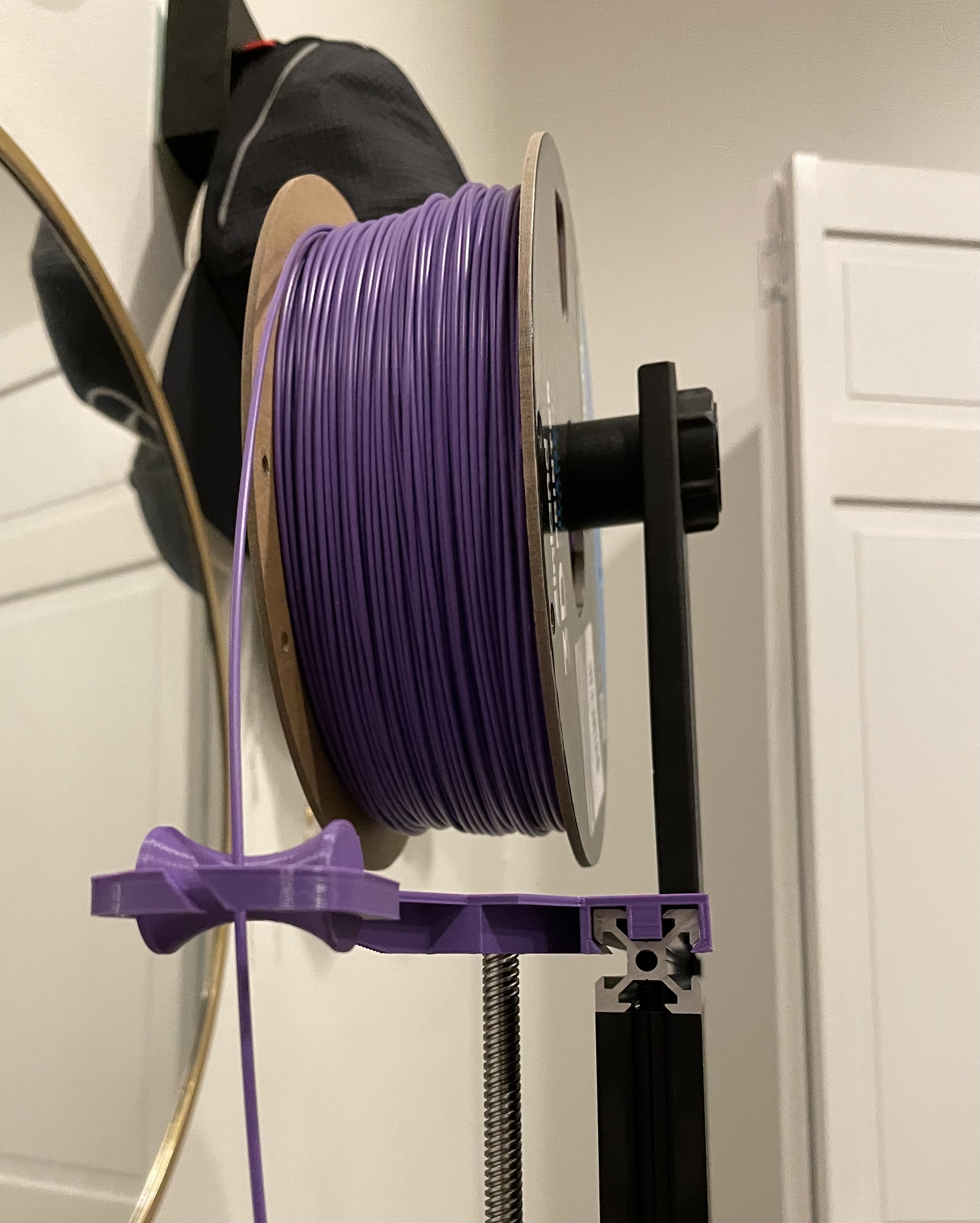 A spool of filament mounted on top of a 3D printer.  The filament is directed through an arm that's attached to the printer.