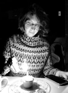 A woman, dramatically lit by the match she's holding to light a candle on a cupcake