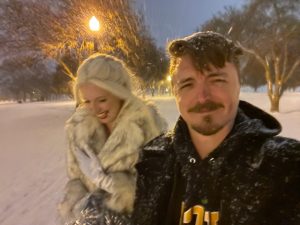 I'm squinting at the camera through the snow; M's wearing a fancy fir coat and a wig beside me.  It's dark, snowy in the park, and actively snowing.