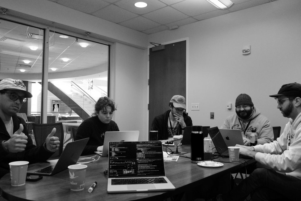 The hackathon team all in front of laptops. Daniel, the man on the left, gives two thumbs up. My laptop is open, facing the camera.