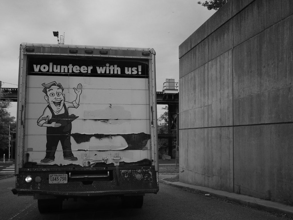 The back of a box truck next to the Richmond flood wall.  The truck reads "volunteer with us!" and there's a cartoon man on the back.  It's slightly sinister!